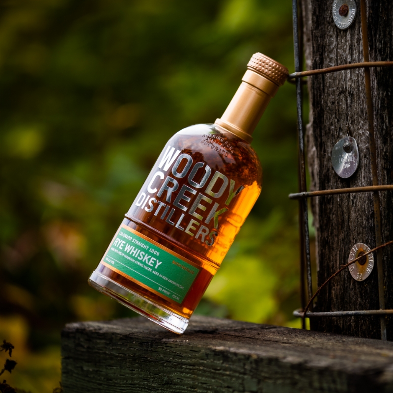 woody creek bottle leaning against fence post