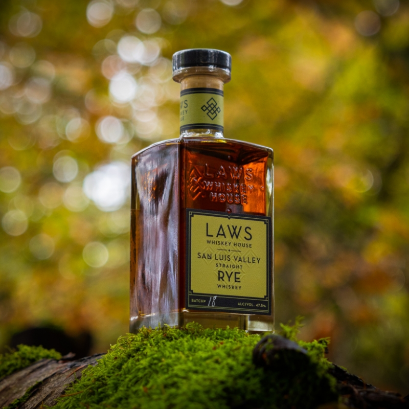 laws whiskey house bottle with a green label sitting on green moss with foliage in the background