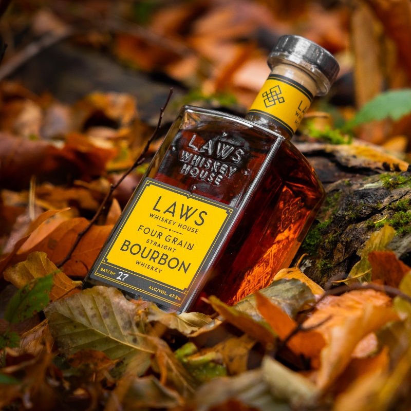 laws whiskey house bottle leaning against a tree branch sitting in colorful leaves