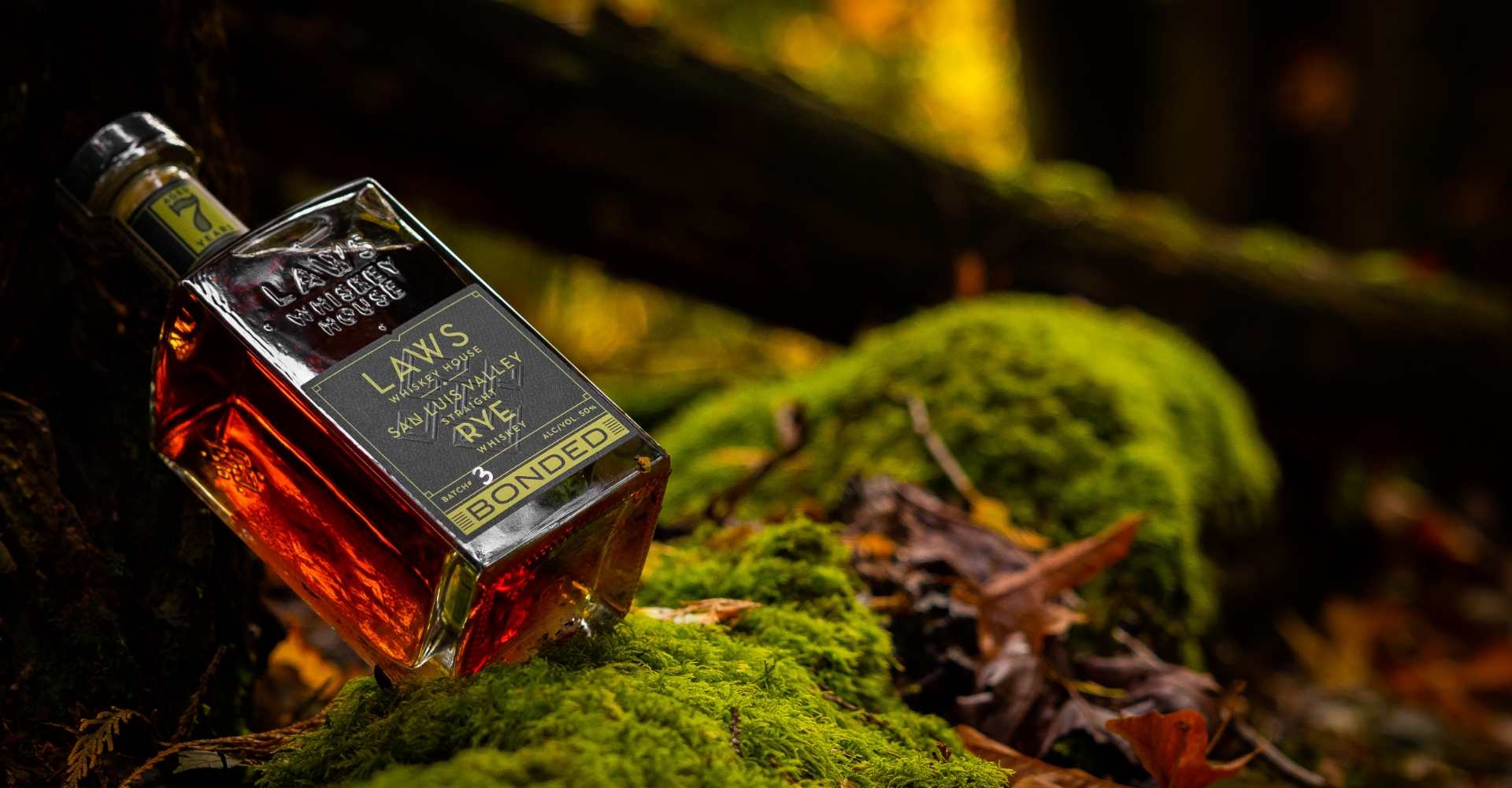 LAWS WHISKEY38 laws whiskey house bottle leaning against a tree stump sitting on green moss