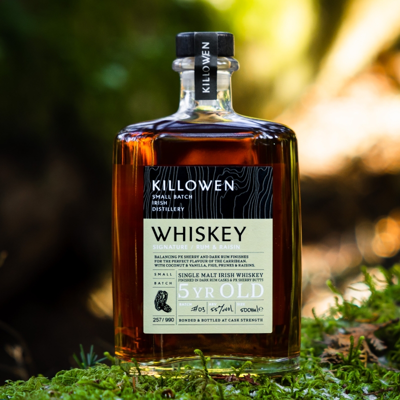 killowen signature rum and raisin whiskey on a piece of wood with green leaves in the background