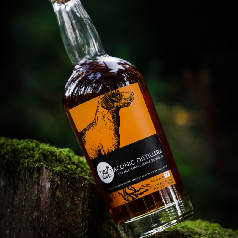 taconic distillery double barrel maple bourbon leaning against a mossy wooden tree stump