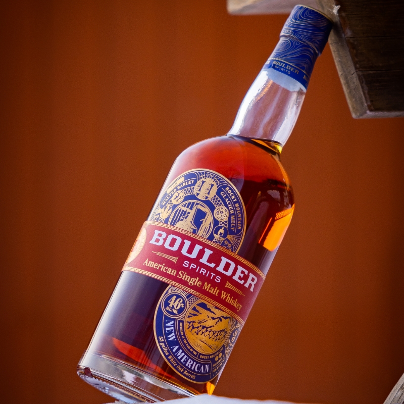 BOULDER ASM5 boulder spirits american single malt whiskey bottle leaning against wood with red background