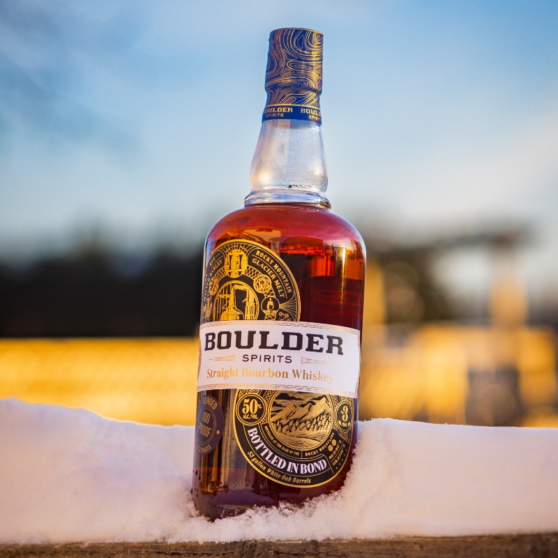 boulder spirits straight bourbon whiskey bottled in bond bottle sitting in snow with a sunset in the background