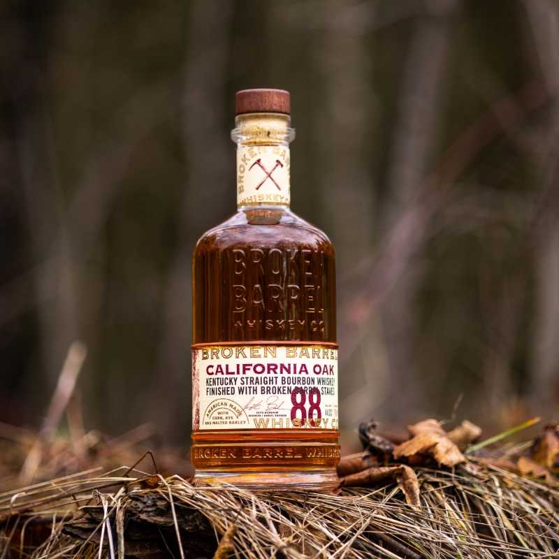 Broken Barrel California Oak bottle sitting on a pile of leaves and grass with brown foliage in the background